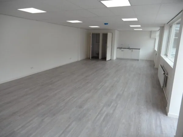 Lichte, lege kantoorruimte aan de Jacques Perkstraat met grijze vloer, systeemplafond en een kleine keuken.